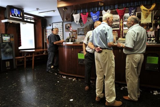 People drink at a bar, as masked members of the Basque separatist militant group ETA are seen delivering a statement on a television, left, in the Basque town of Hernani, northern Spain, on Sept. 5.